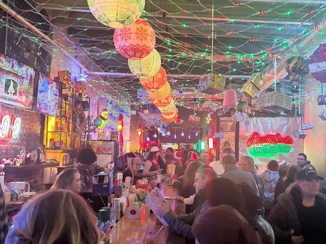 A packed One Fourteen bar during Sippin' Santa 2025, ceiling hung with lanterns and lights